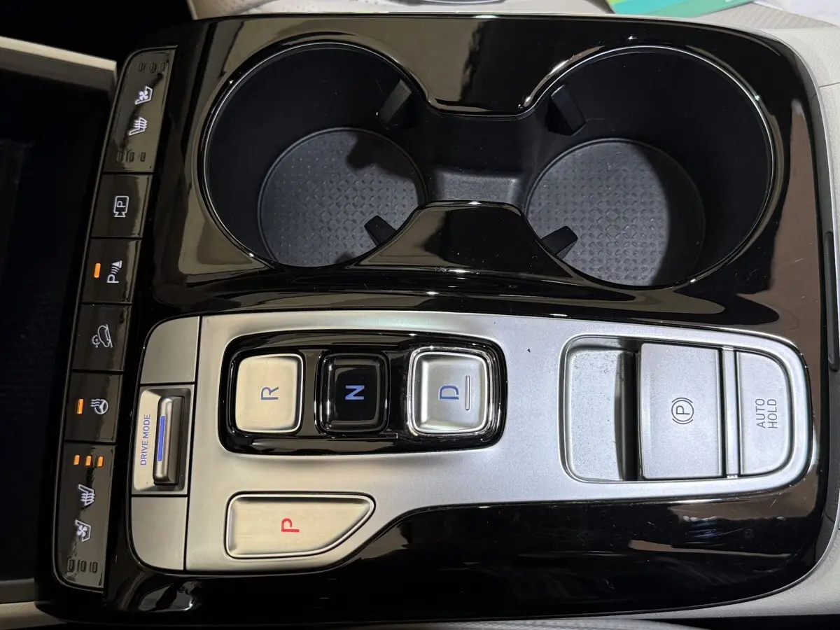 Vue rapprochée de la console centrale noire et argentée du Hyundai Tucson 1.6 Hybrid 230 Executive avec commandes de boîte auto et porte-gobelets.