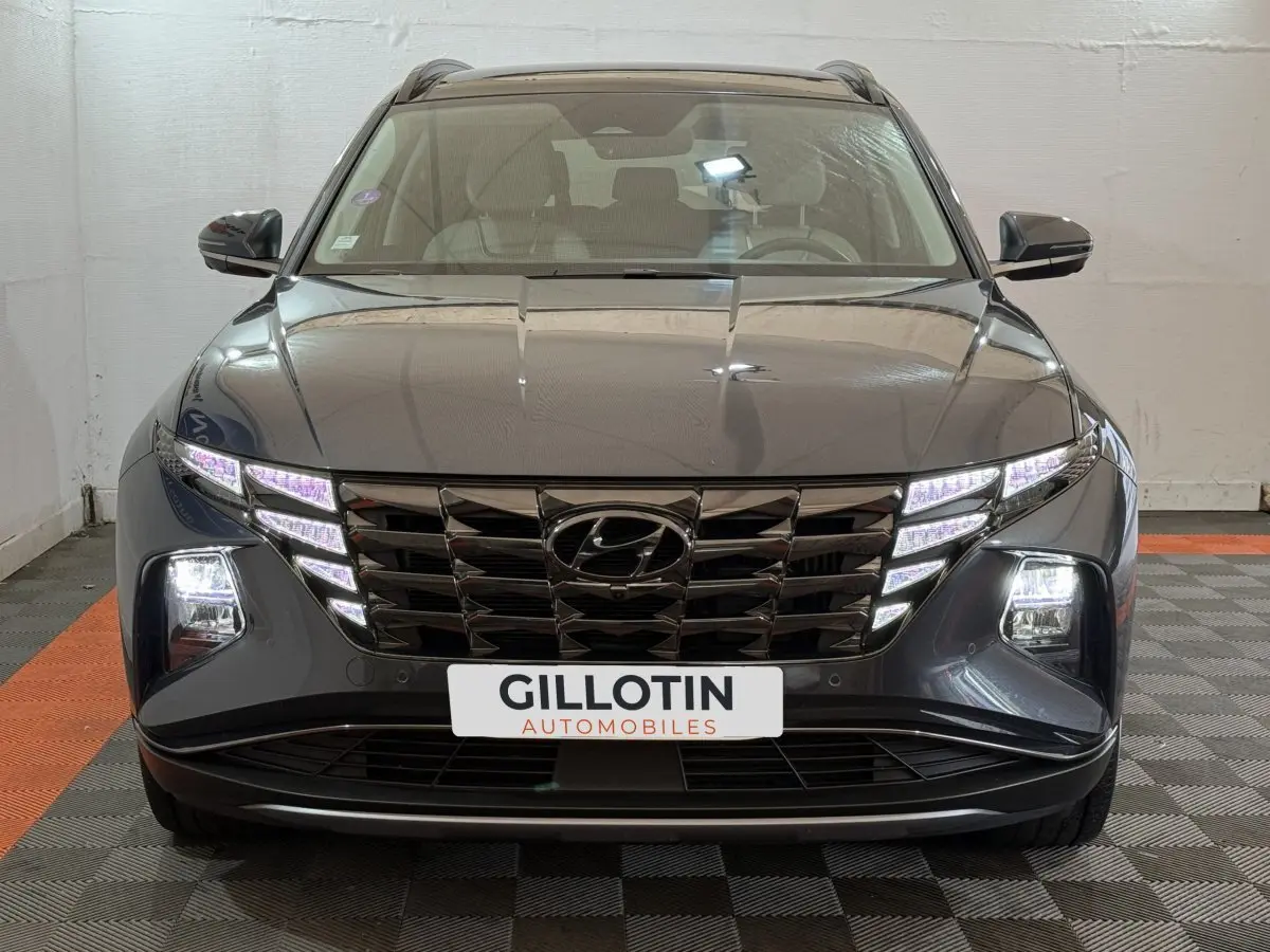 Vue frontale d’un Hyundai Tucson gris foncé avec calandre noire et feux LED allumés en intérieur.