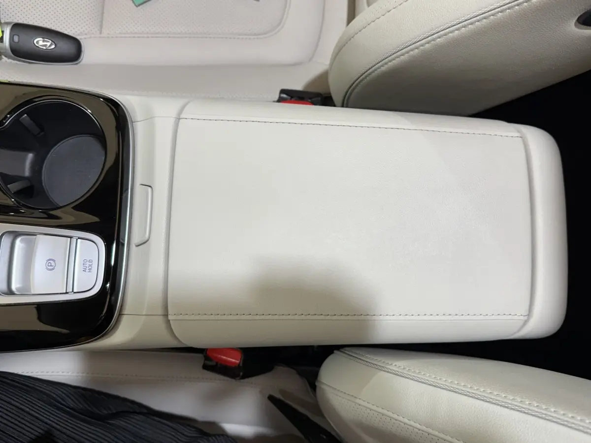 Vue rapprochée de la console centrale beige clair du Hyundai Tucson 1.6 Hybrid 230 Executive avec commandes de frein et porte-gobelet.