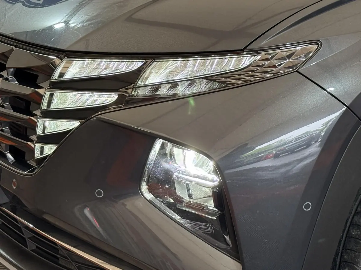 Gros plan sur l'avant droit gris foncé du Hyundai Tucson 1.6 Hybrid 230 Executive, mettant en valeur les phares LED et la calandre.