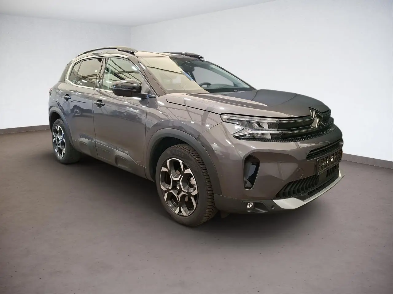 Vue 3/4 avant droit du Citroën C5 Aircross gris Platinium avec jantes alliage bi-ton et barres de toit noires.