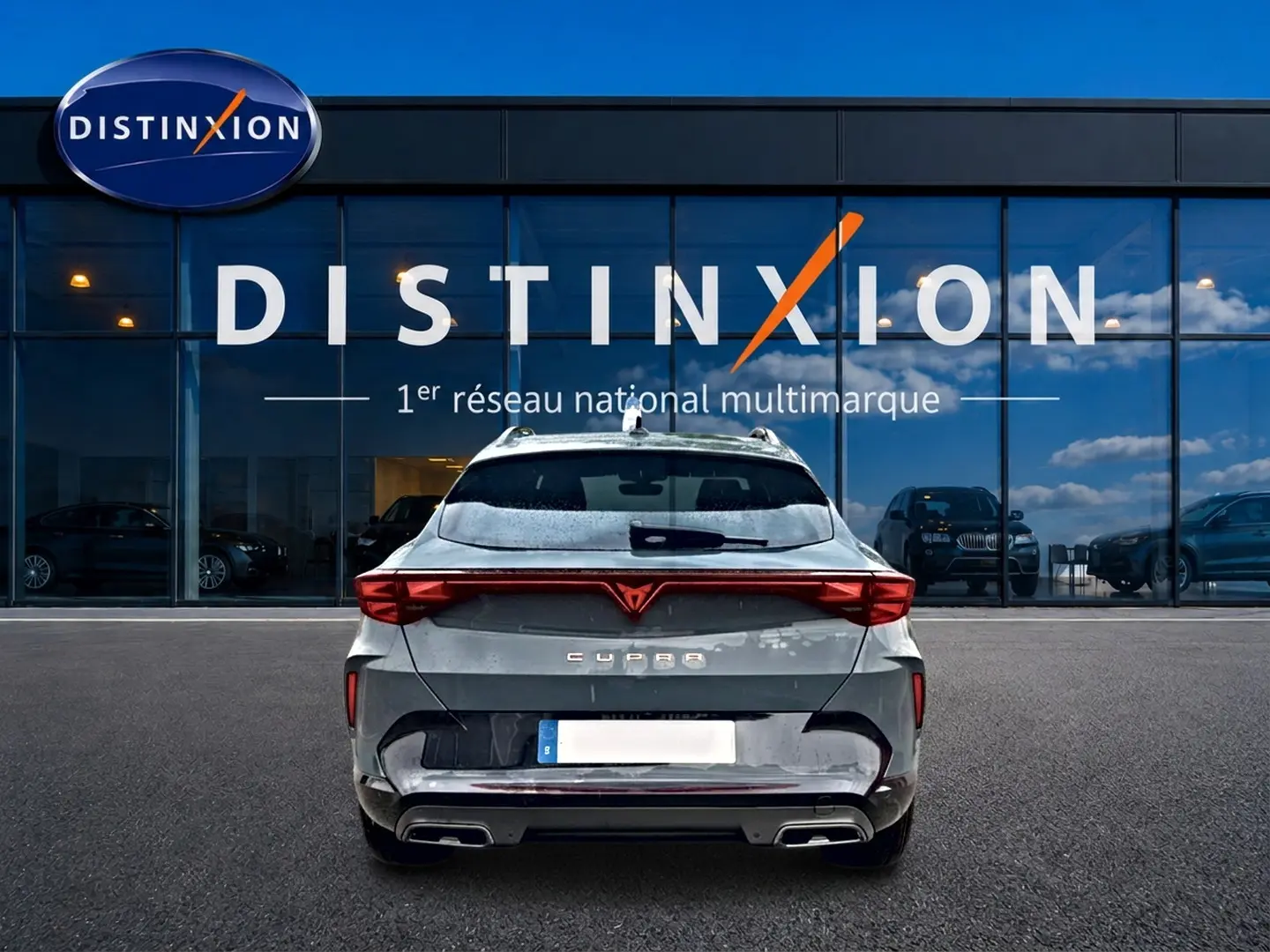 Vue arrière d'un CUPRA Formentor bleu fjord 2026 avec feux LED et double sortie d'échappement, devant un showroom Distinxion.