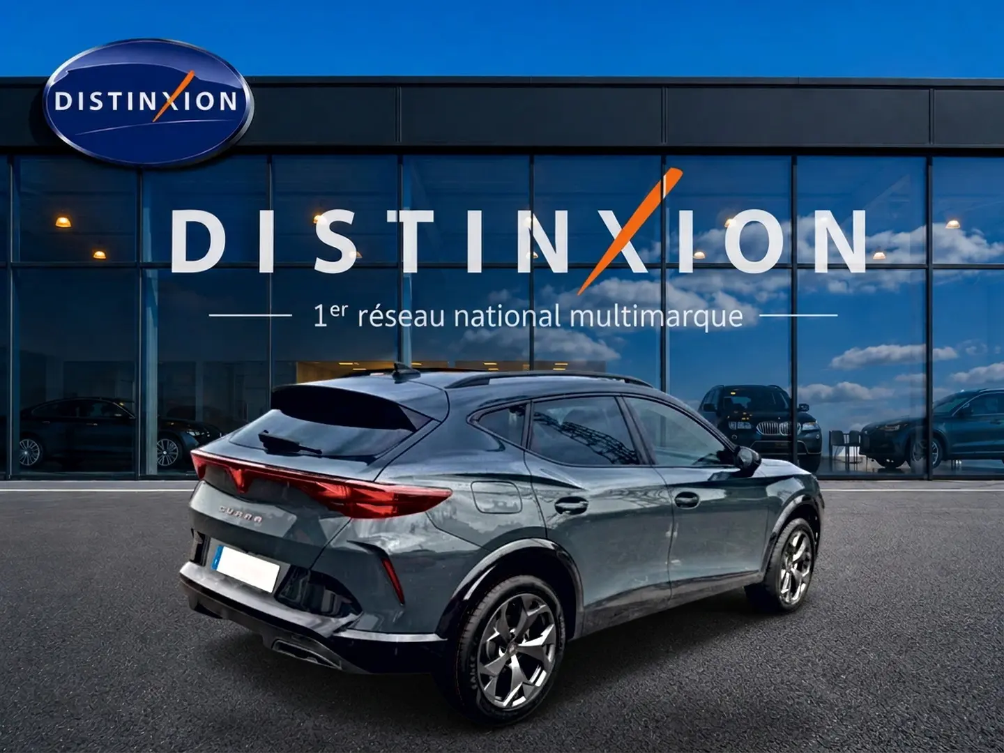 Vue 3/4 arrière droite d'une CUPRA Formentor bleu fjord avec feux arrière LED et jantes 18 pouces devant un showroom Distinxion.