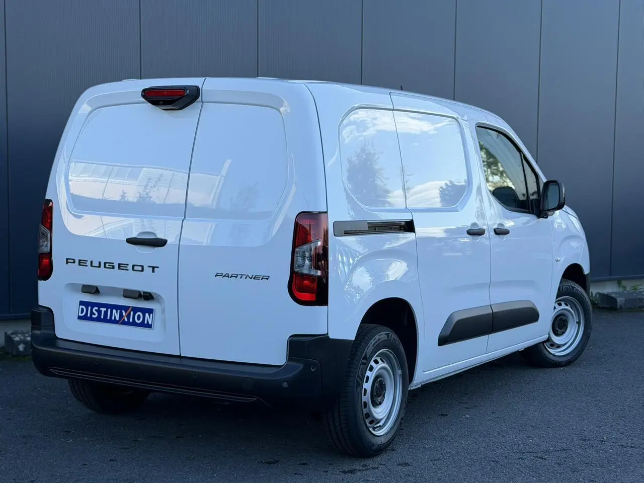 Vue 3/4 arrière droite d'un Peugeot Partner blanc Icy avec portes arrière battantes et protections latérales noires.