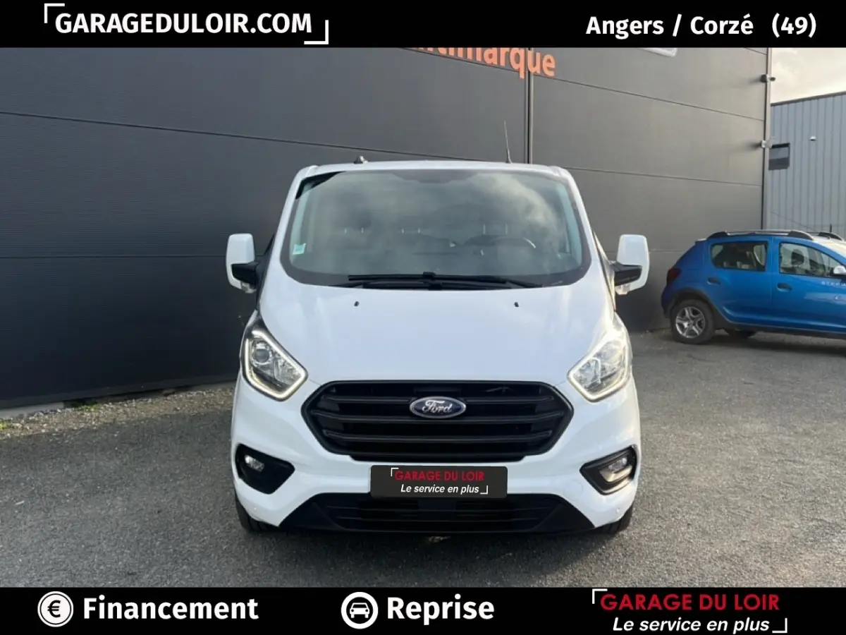 Vue frontale d'un Ford Transit Custom Fourgon blanc 2023 avec calandre noire et phares allumés.