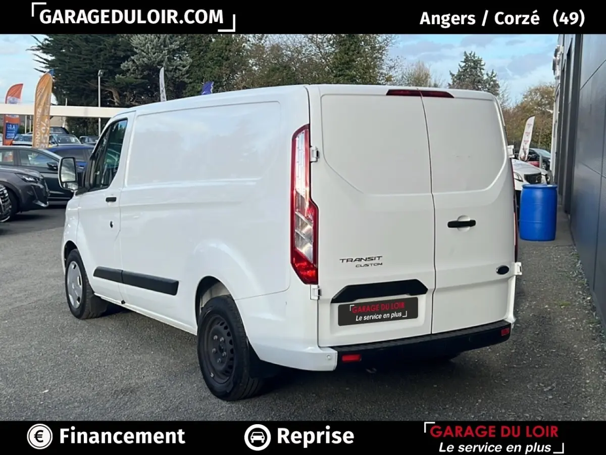 Vue 3/4 arrière droite d’un fourgon Ford Transit Custom blanc avec portes arrière fermées sur parking extérieur.