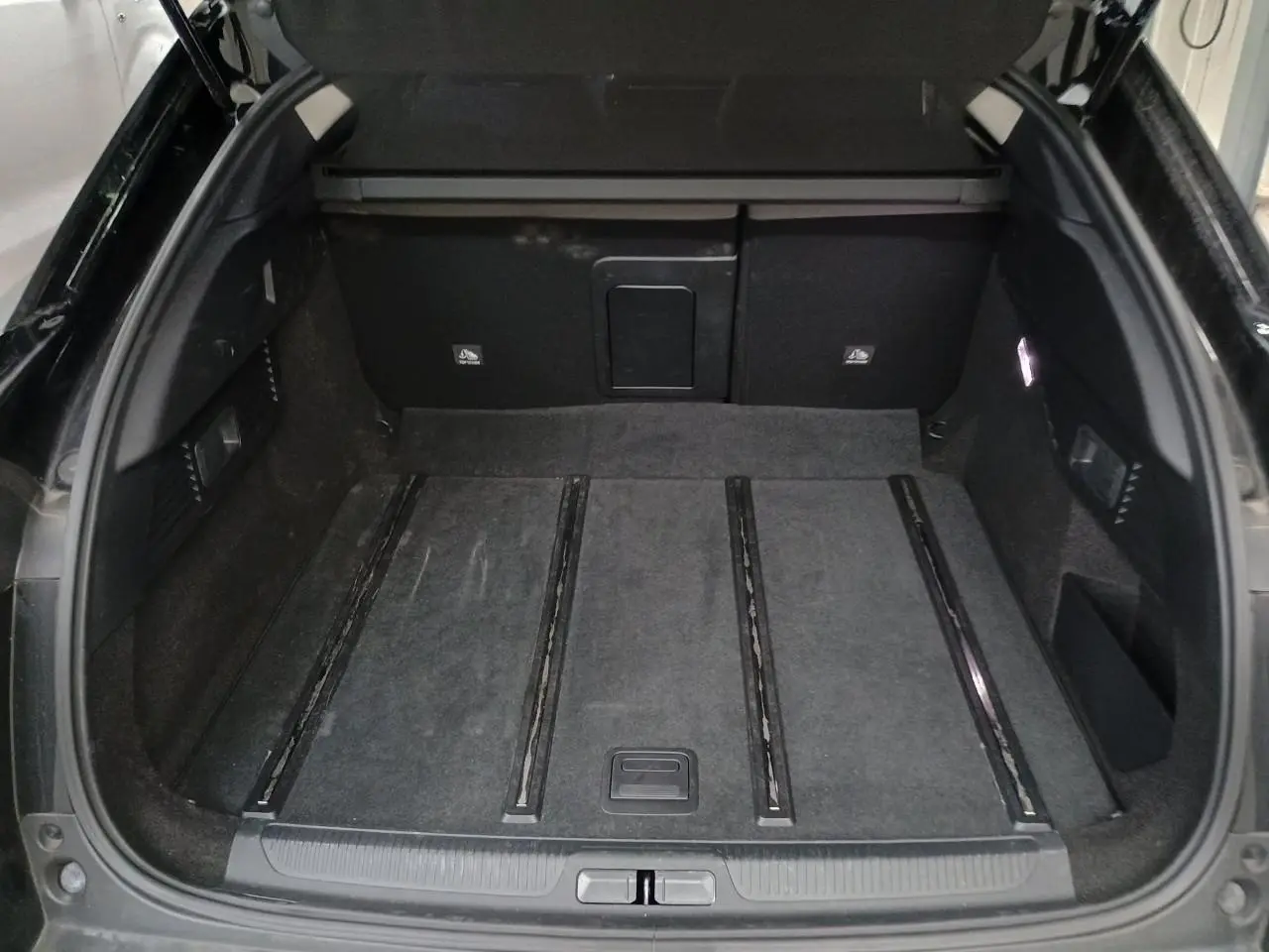 Coffre ouvert vu de l'arrière d'une Citroën C5 X Noir Perla, avec tapis de sol et rangements latéraux visibles.