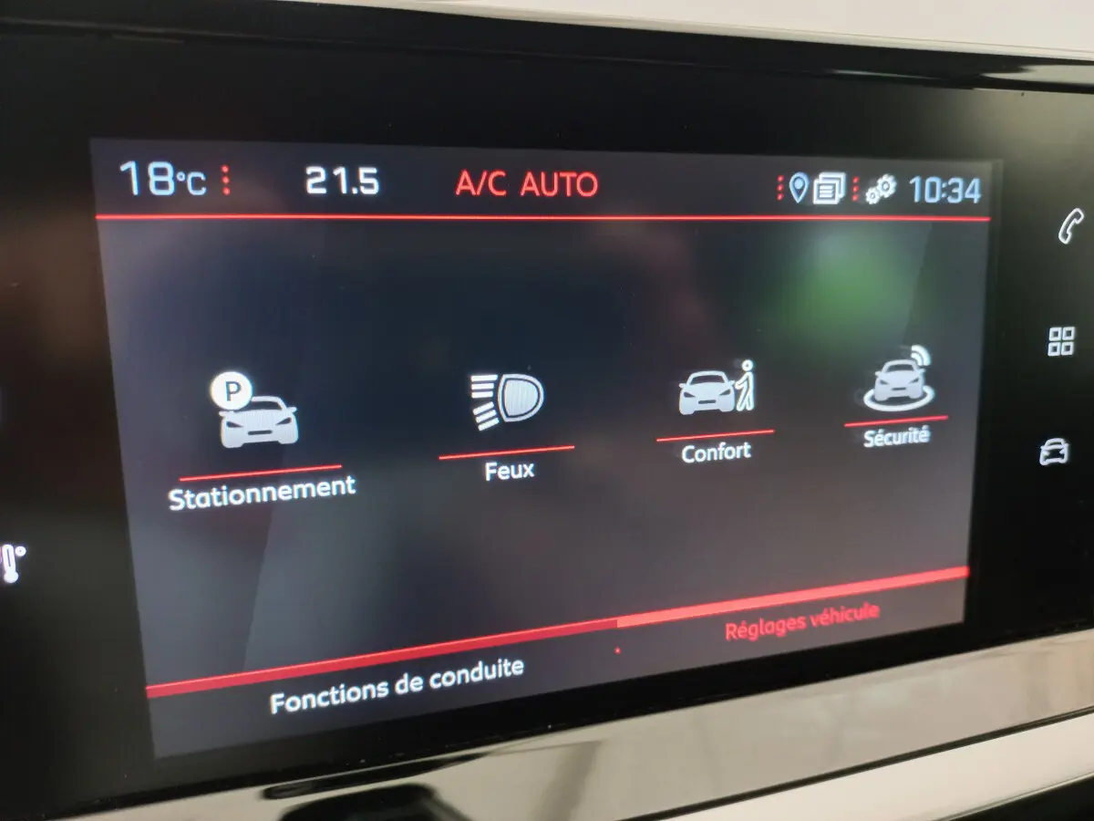 Écran tactile intérieur de la Peugeot 208 blanc, affichant les réglages de stationnement, feux, confort et sécurité.