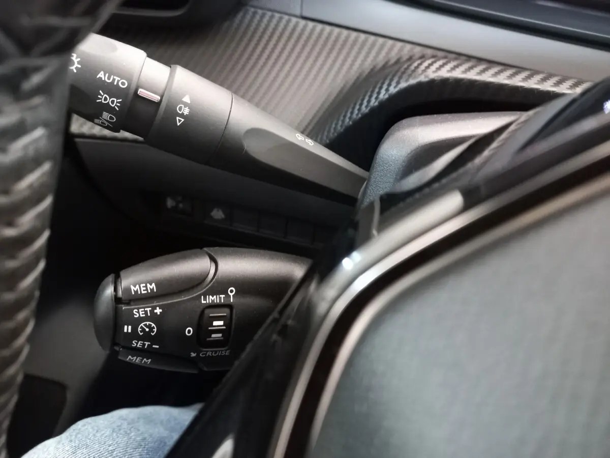 Gros plan sur les commandes de régulateur de vitesse et éclairage du tableau de bord intérieur d'une Peugeot 208 blanche.