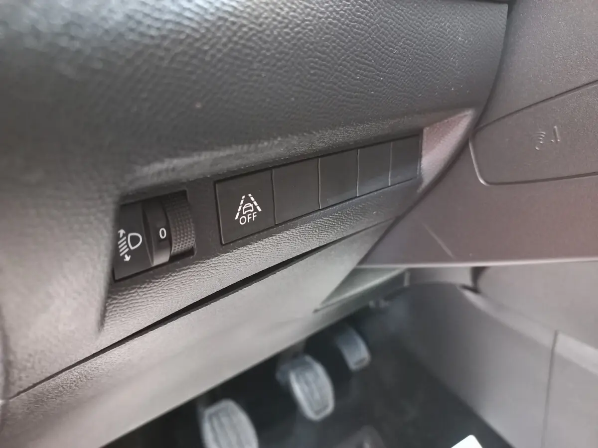 Gros plan sur les commandes de réglage des phares et désactivation de l’assistance au maintien de voie dans une Peugeot 208 blanche.
