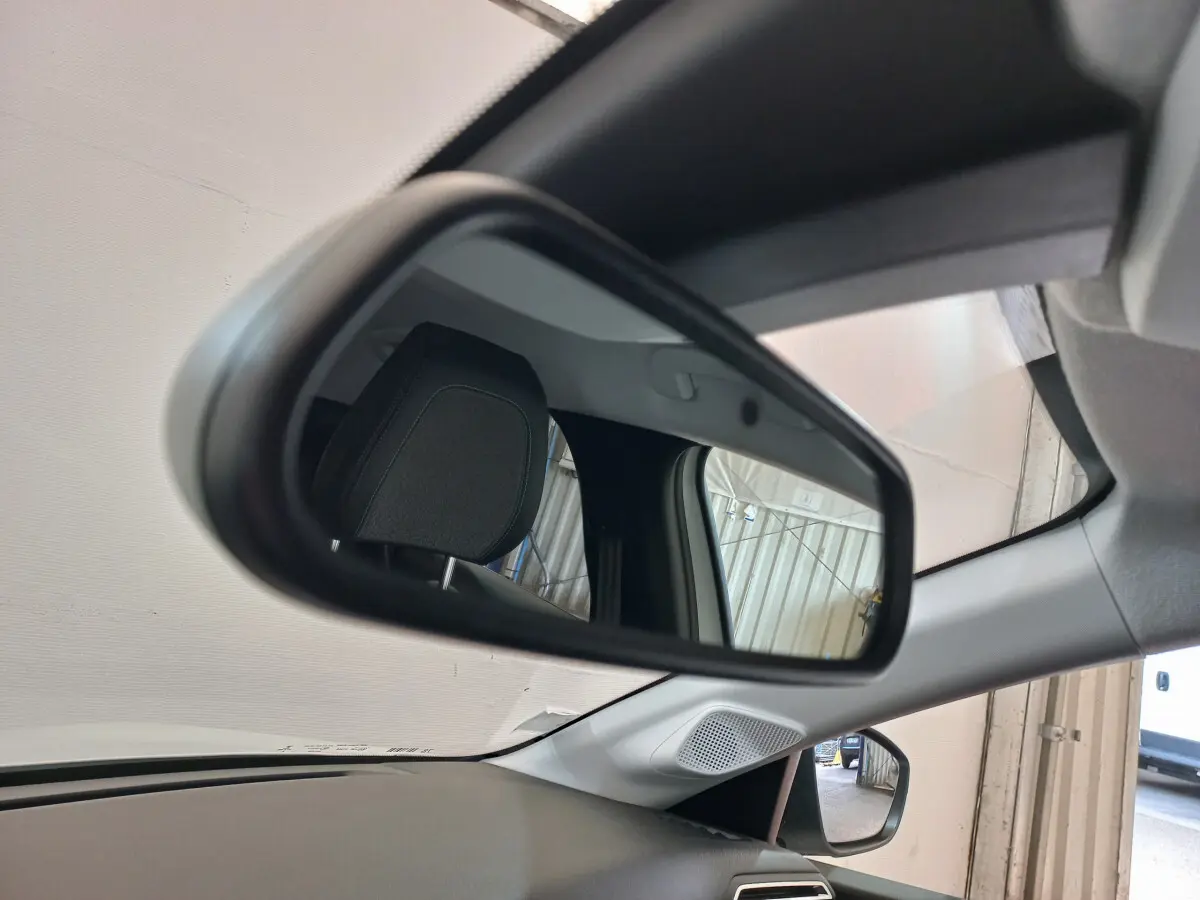 Vue intérieure du rétroviseur gauche d'une Peugeot 208 blanche 2021, avec appui-tête et partie du tableau de bord visibles.