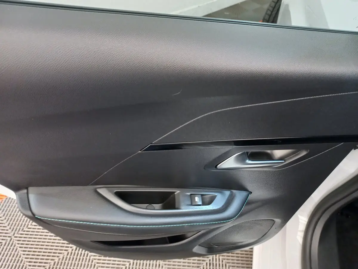 Vue rapprochée de la porte avant gauche noire de la Peugeot 208 blanche, avec poignée argentée et bouton de verrouillage.