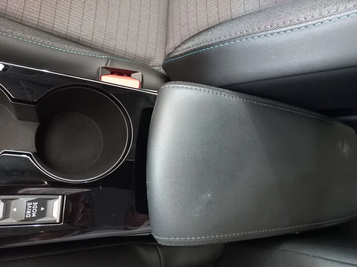 Vue rapprochée de l'accoudoir en cuir noir et du porte-gobelet central de la Peugeot 208 PureTech 100 S&S Allure.