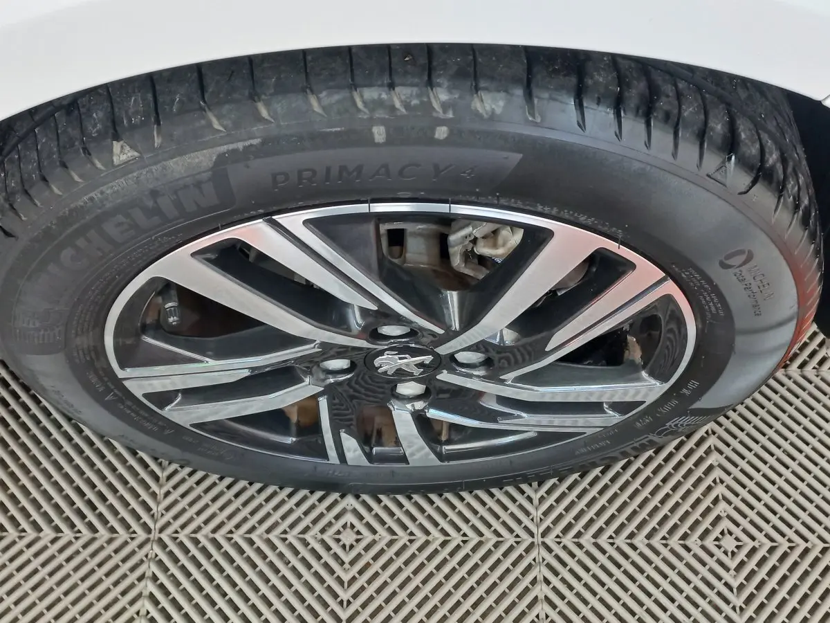 Gros plan sur la roue avant droite d'une Peugeot 208 blanche, jante alliage noire et argent avec logo lion central.