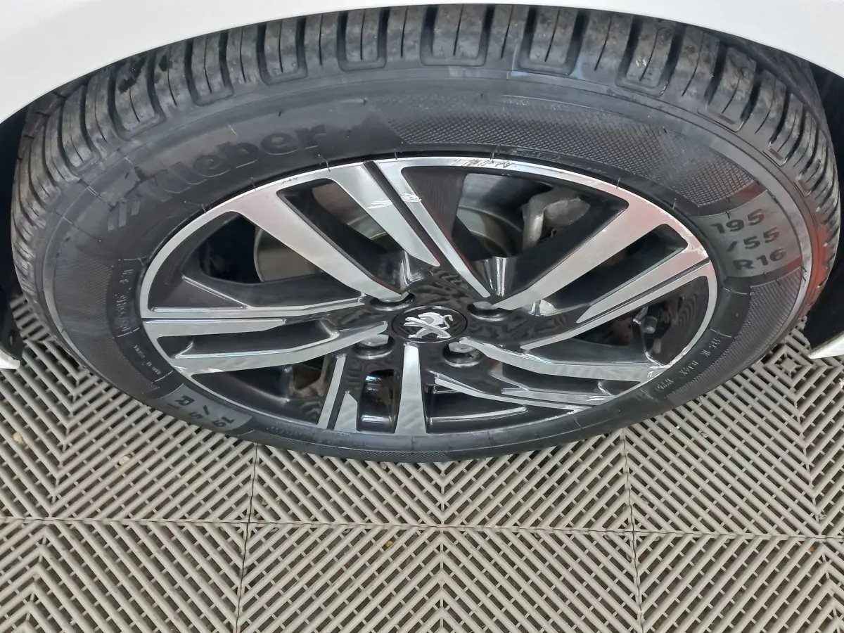 Gros plan sur la roue avant droite de la Peugeot 208 blanche, mettant en valeur la jante alliage bicolore et le pneu Kleber.