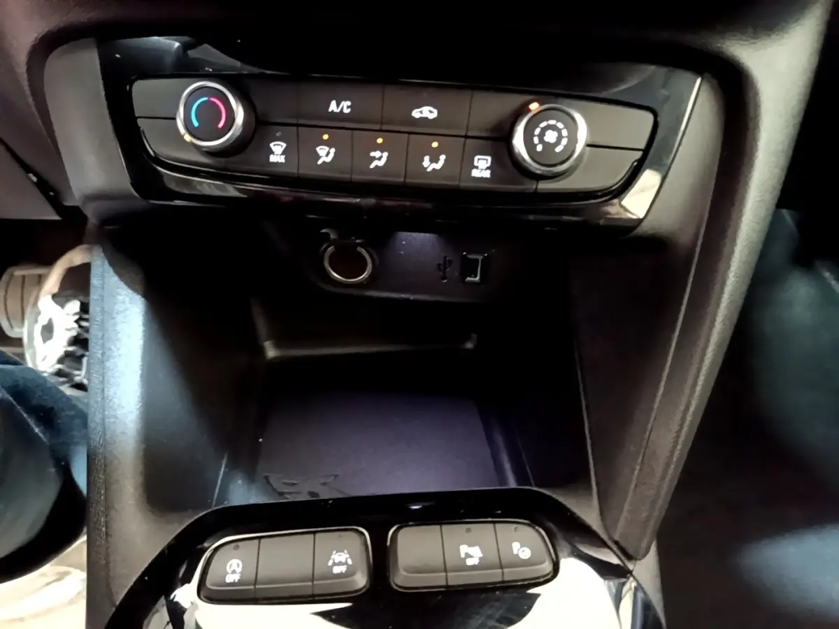 Vue rapprochée du tableau de bord et console centrale noire de l’Opel Corsa blanche, avec commandes climatisation et ports USB visibles.