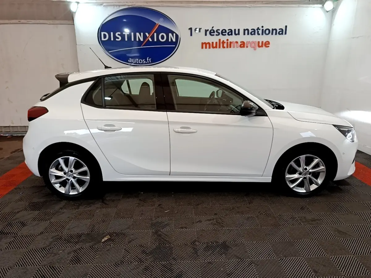 Vue latérale droite d'une Opel Corsa blanche 2023 avec spoiler de toit et jantes alliage en intérieur showroom.