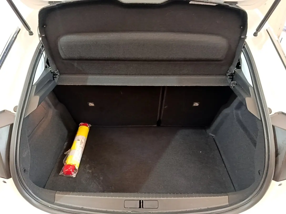 Coffre ouvert d’une Opel Corsa blanche, vue de l’arrière montrant un espace de chargement vide avec un triangle de signalisation.
