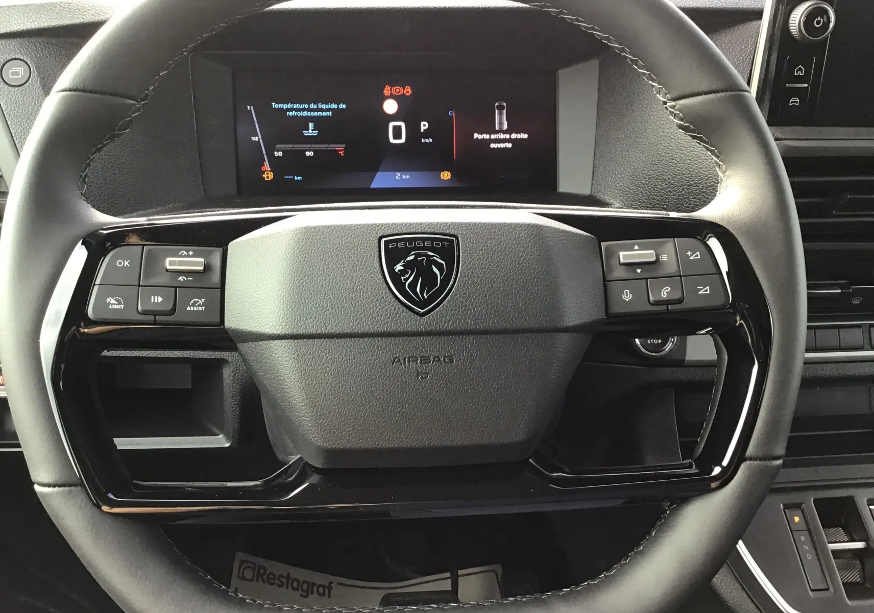 Vue rapprochée du volant noir du Peugeot Expert XL avec commandes intégrées et tableau de bord digital affichant des alertes.