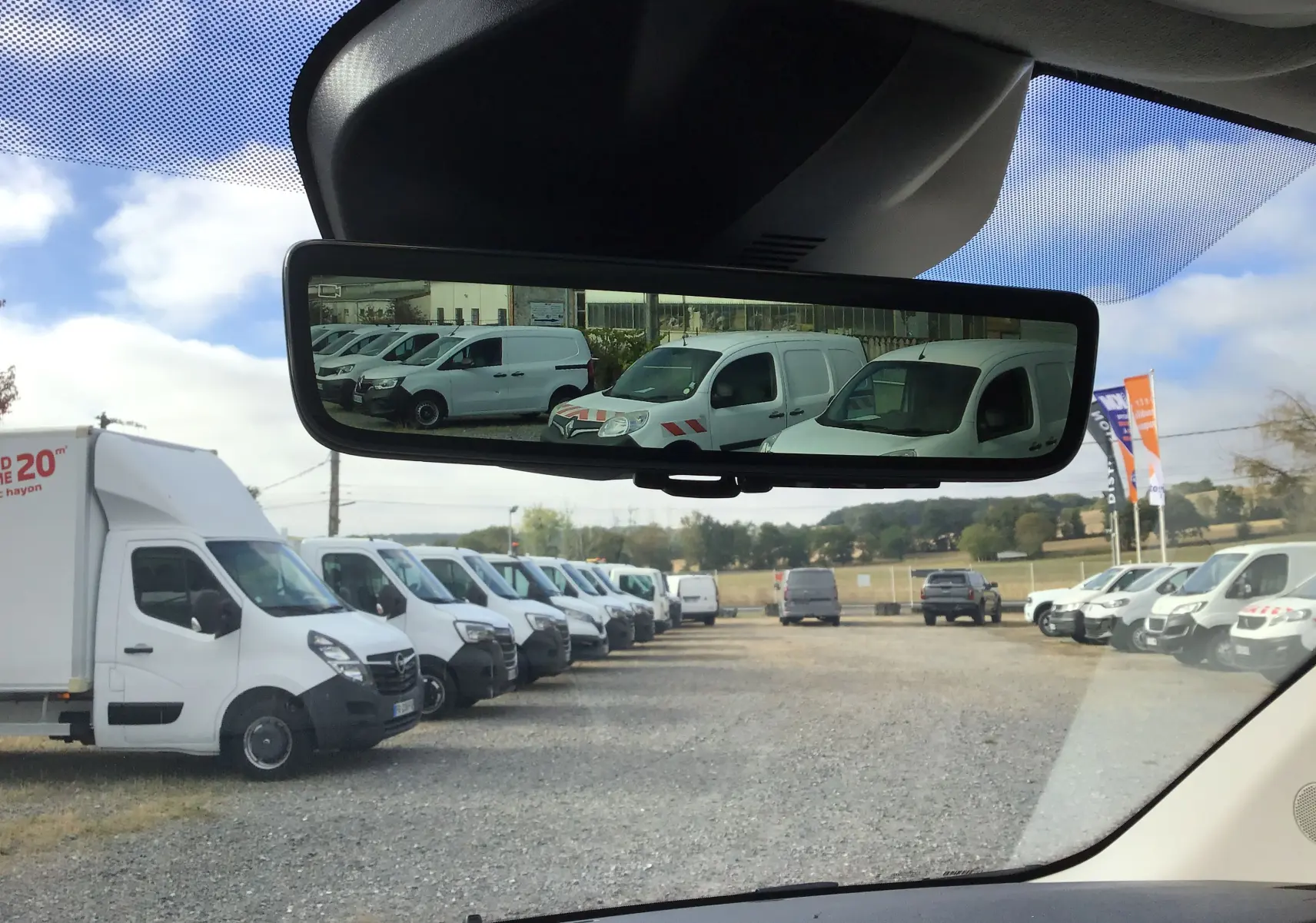 Vue depuis l'intérieur vers l'arrière, reflet dans le rétroviseur d'une rangée de véhicules utilitaires blancs, PEUGEOT Expert noir non visible.