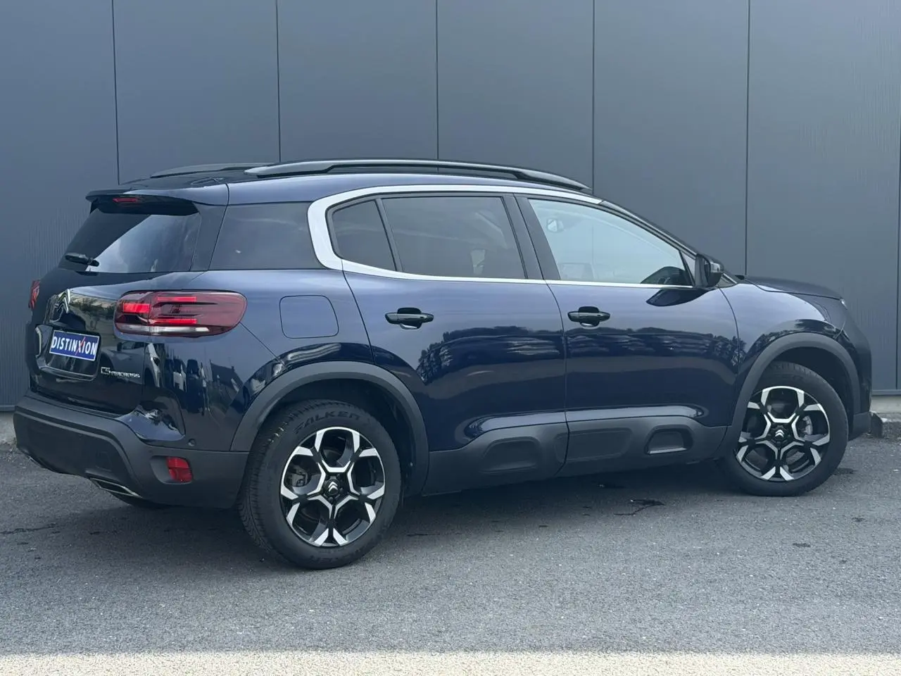 Vue 3/4 arrière droite d'un Citroën C5 Aircross Bleu Eclipse avec jantes alliage bi-ton et barres de toit noires.