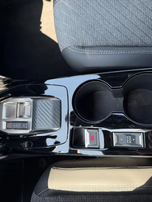 Vue rapprochée de la console centrale noire brillante du Peugeot 2008 Hybrid 145 Allure avec boutons Drive Mode et frein à main électronique.