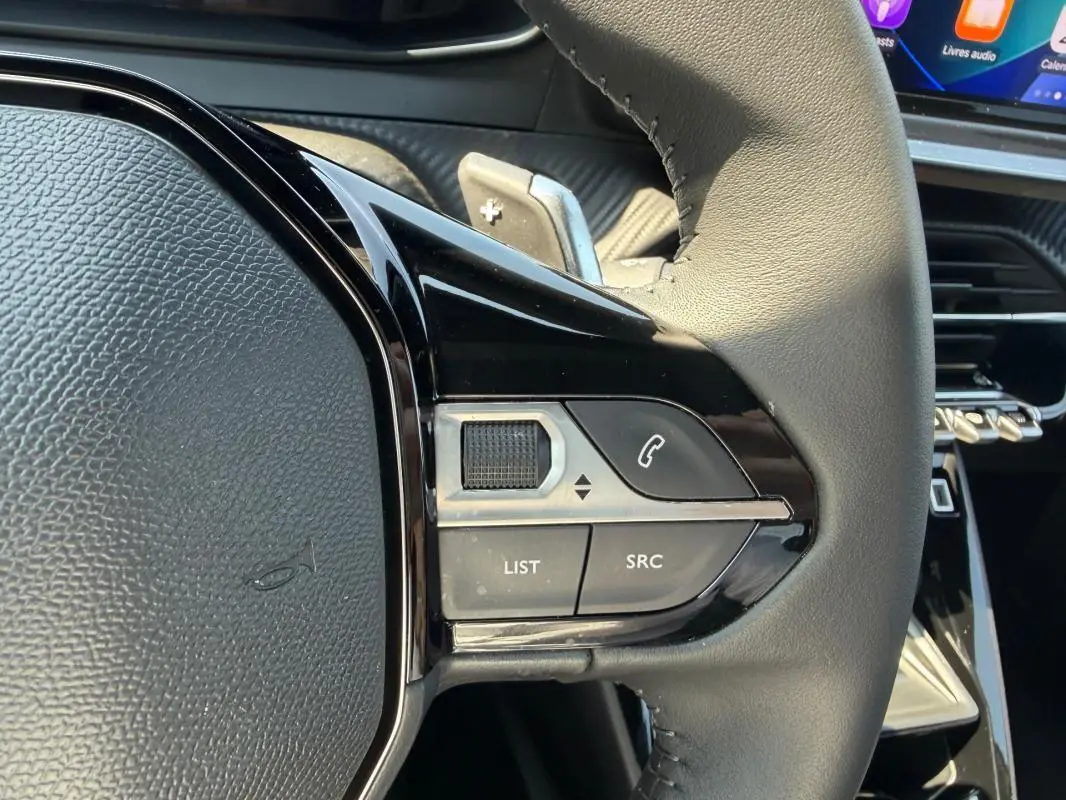Gros plan sur la partie droite du volant du Peugeot 2008 Hybrid gris, avec commandes audio et téléphone intégrées.
