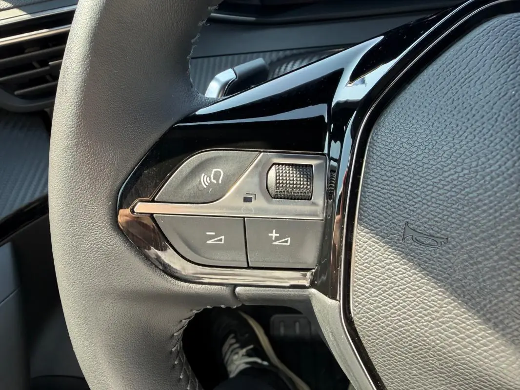 Gros plan sur les commandes gauche du volant gris du Peugeot 2008 Hybrid 145 e-DCS6 Allure 2025, avec boutons de volume et appel.