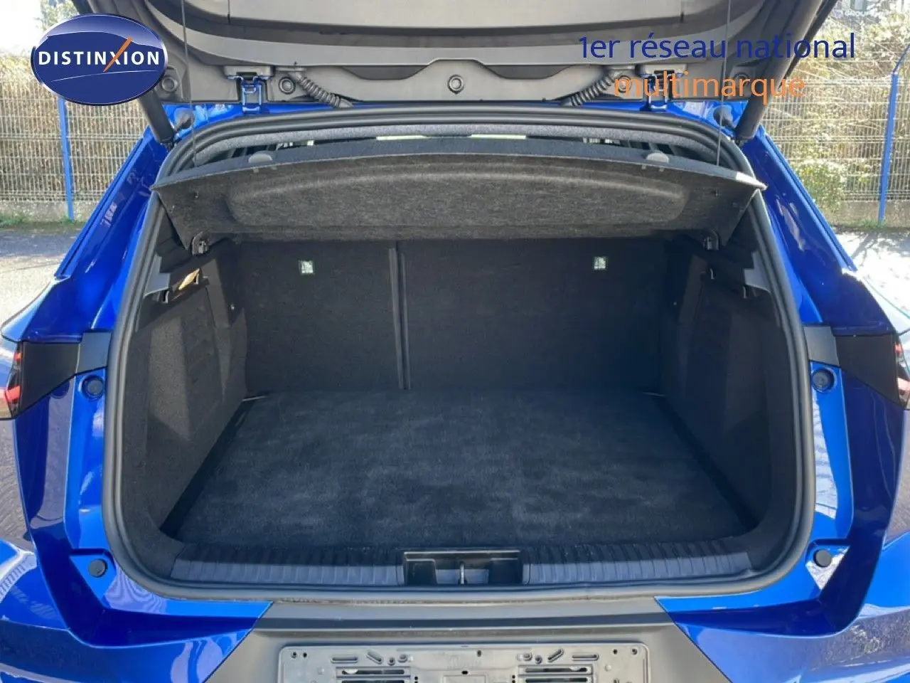 Coffre ouvert vu de l'arrière d'une Renault Symbioz 2025 bleu iron metal, espace de chargement vide et tapis noir.