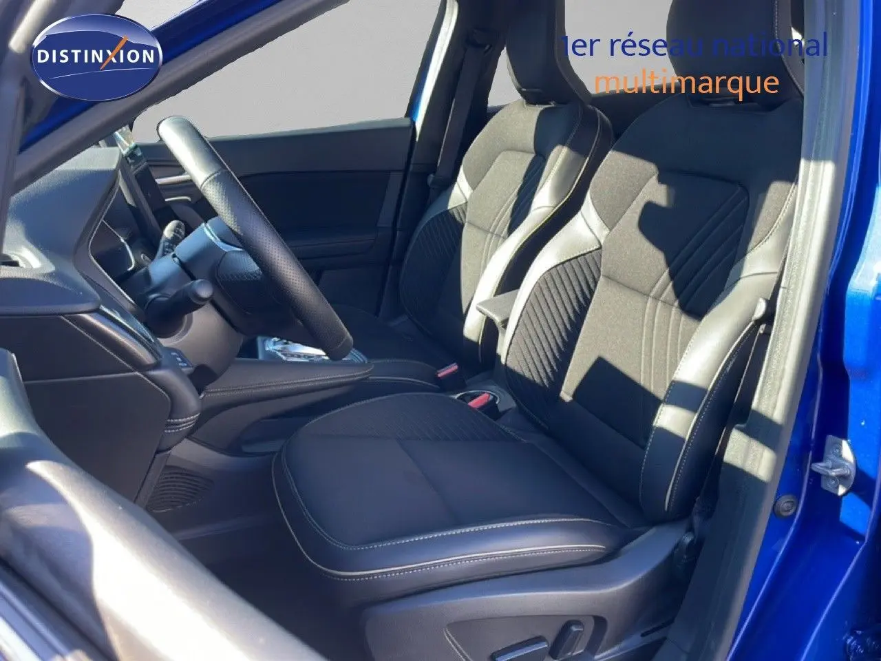 Vue intérieure côté conducteur de la Renault Symbioz 2025 bleu iron metal, sièges tissu et cuir avec surpiqûres blanches.