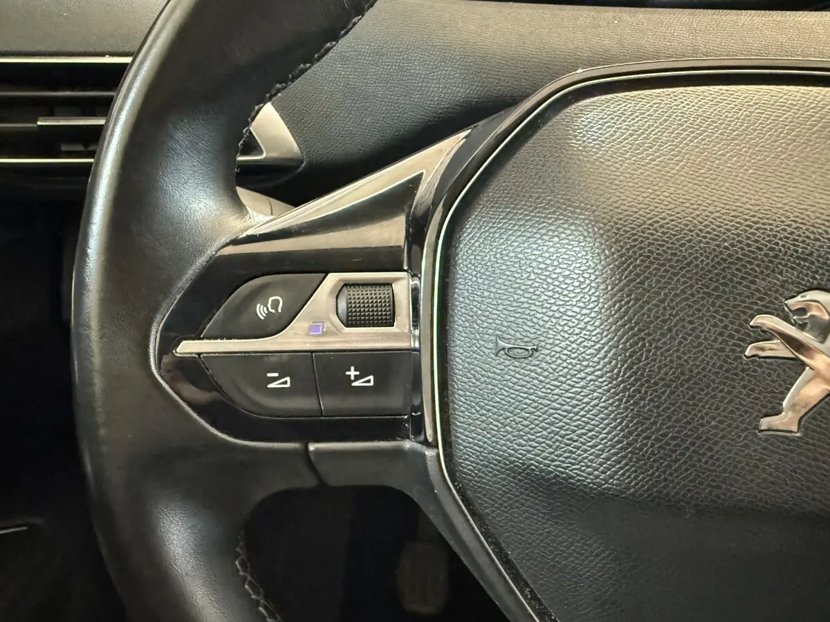 Gros plan sur le volant cuir noir du Peugeot 3008 avec commandes vocales et logo lion central visible.