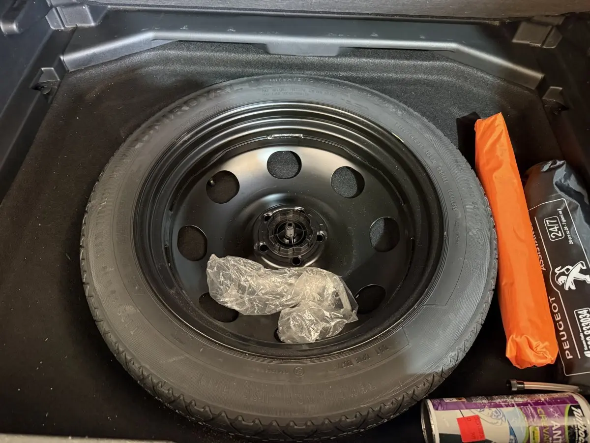 Vue plongeante sur la roue de secours noire dans le coffre d’un Peugeot 3008 vert, avec kit de réparation visible.