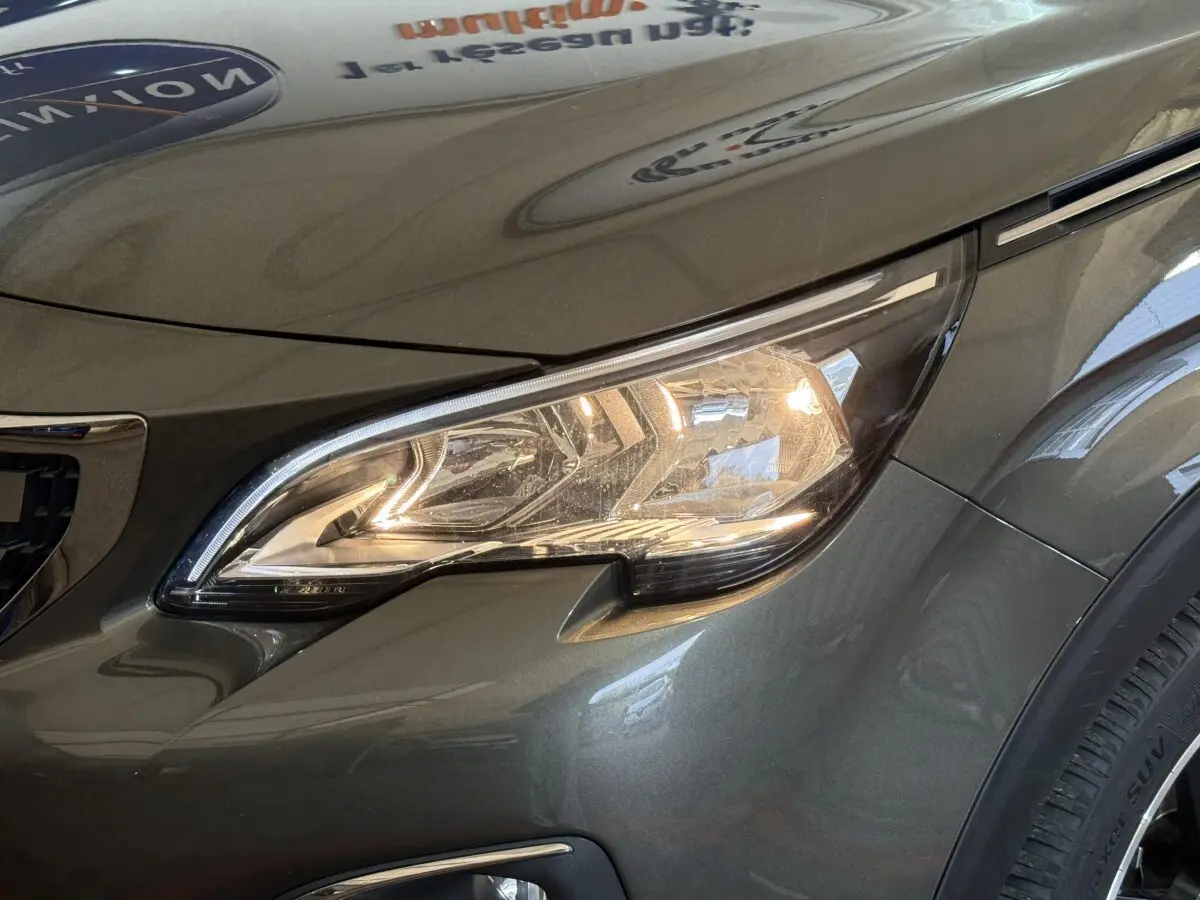 Gros plan sur le phare avant droit du Peugeot 3008 vert métallisé, mettant en valeur ses lignes modernes et le clignotant LED intégré.
