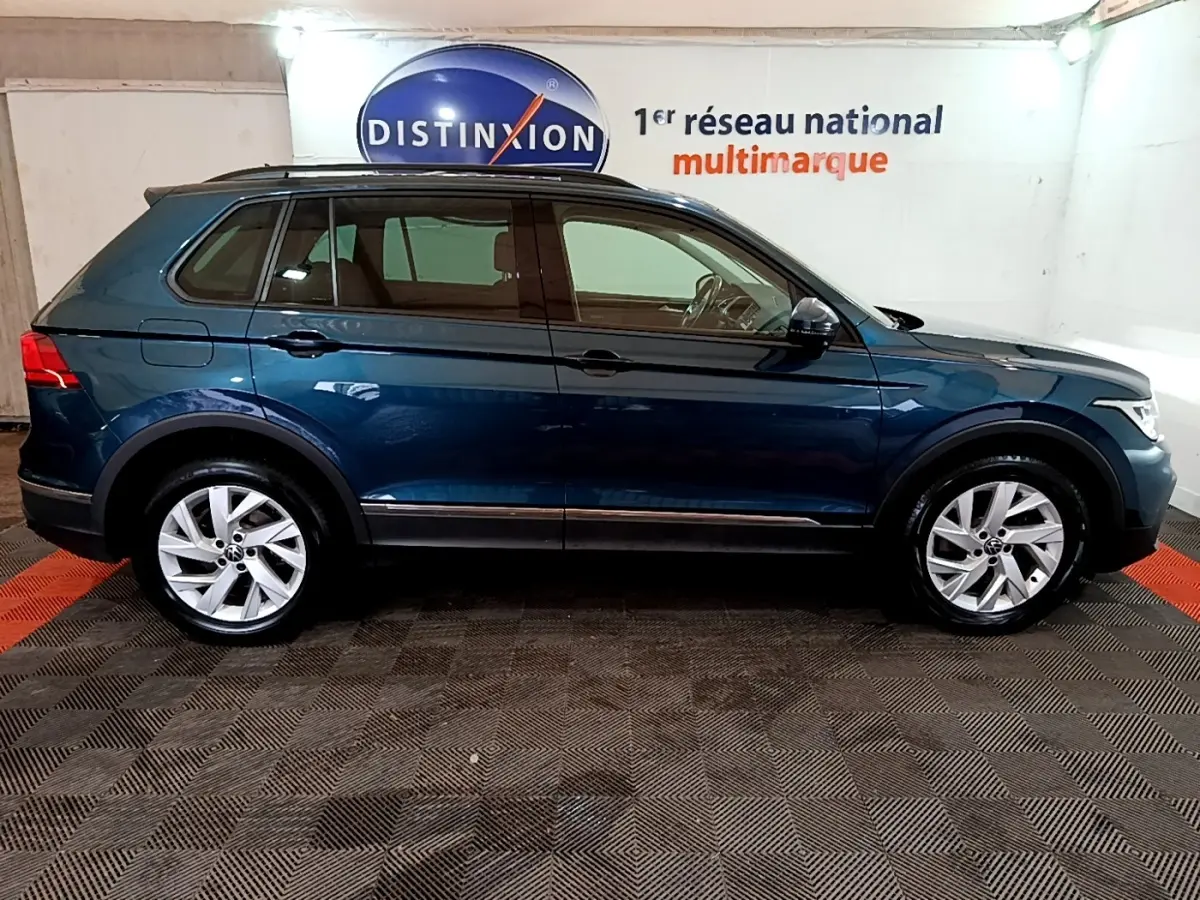Vue de profil côté gauche d’un Volkswagen Tiguan bleu hybride rechargeable dans un showroom intérieur.