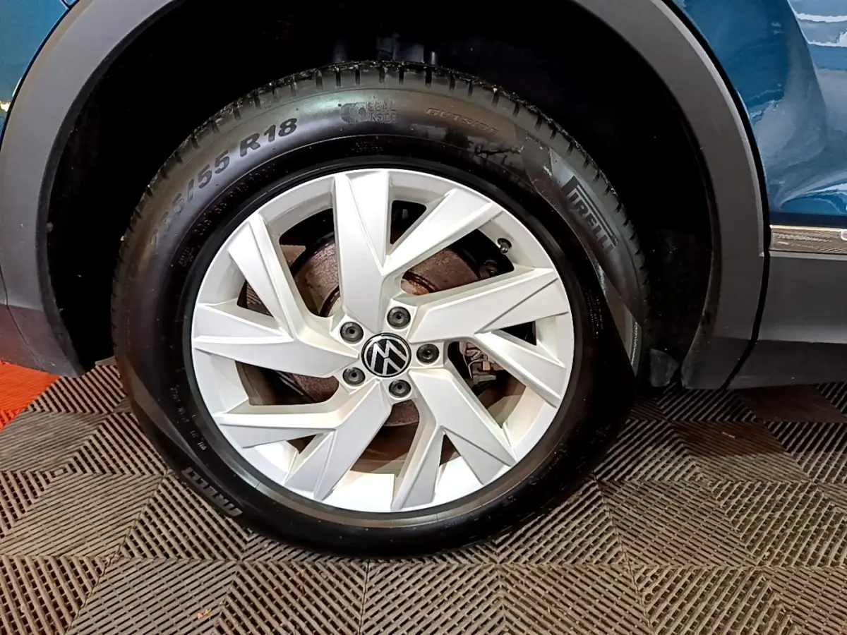 Gros plan sur la roue arrière droite d’un Volkswagen Tiguan bleu, avec passage de roue noir et bas de caisse chromé visible.
