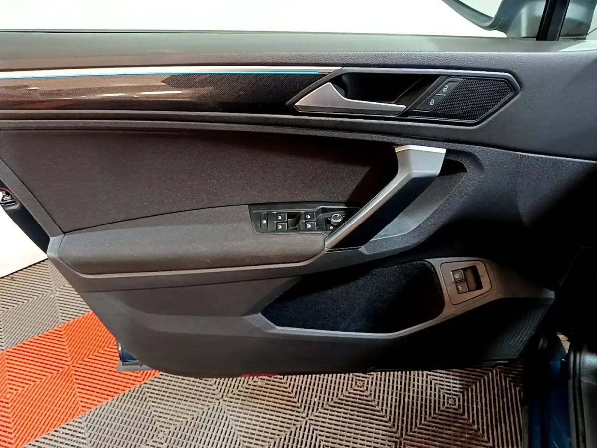 Vue intérieure côté gauche de la porte avant d’un Volkswagen Tiguan bleu, avec commandes électriques et garniture noire.
