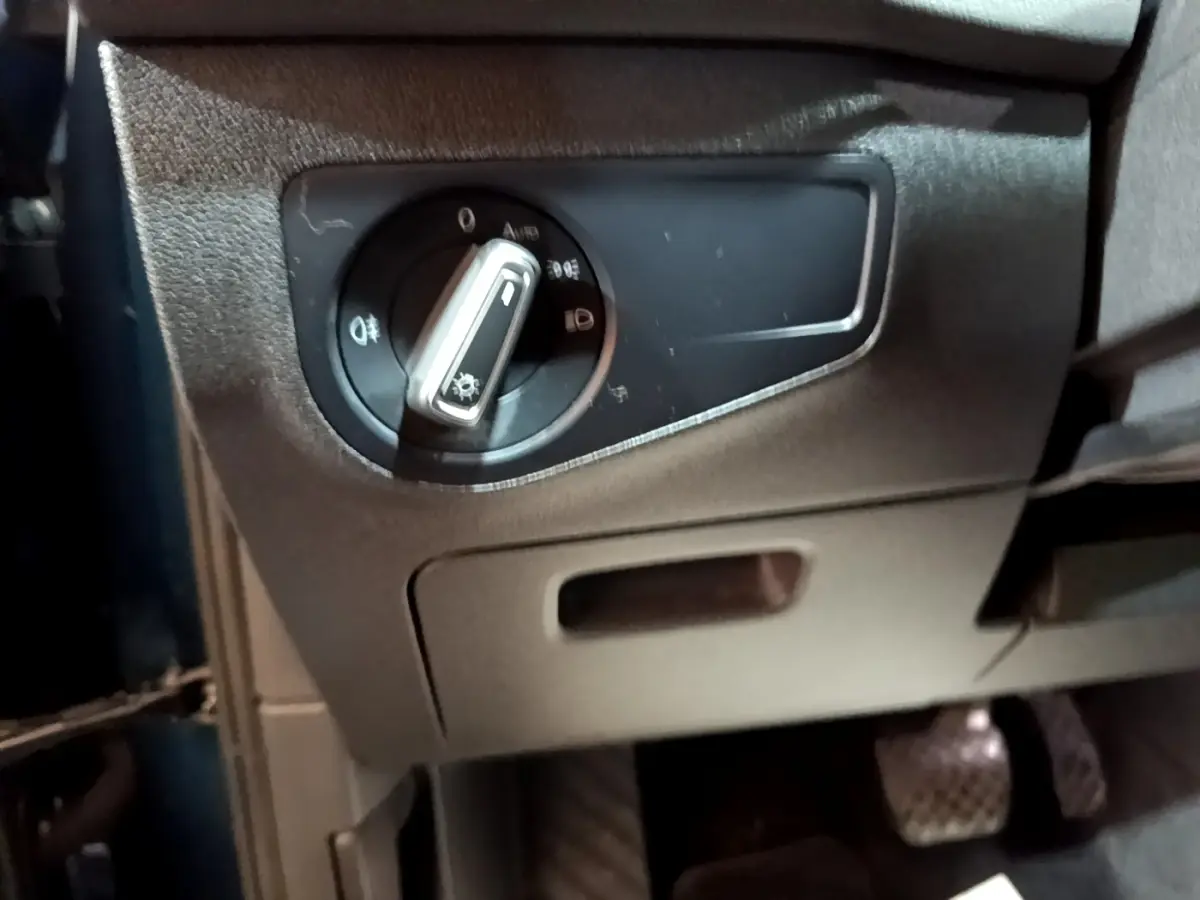 Gros plan sur le bouton de commande des phares noir et argenté, intérieur côté conducteur du Volkswagen Tiguan bleu hybride.