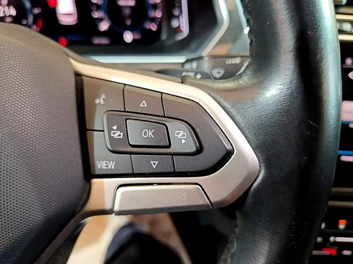 Gros plan sur les commandes multifonctions noires et argent du volant cuir du Volkswagen Tiguan bleu hybride rechargeable.