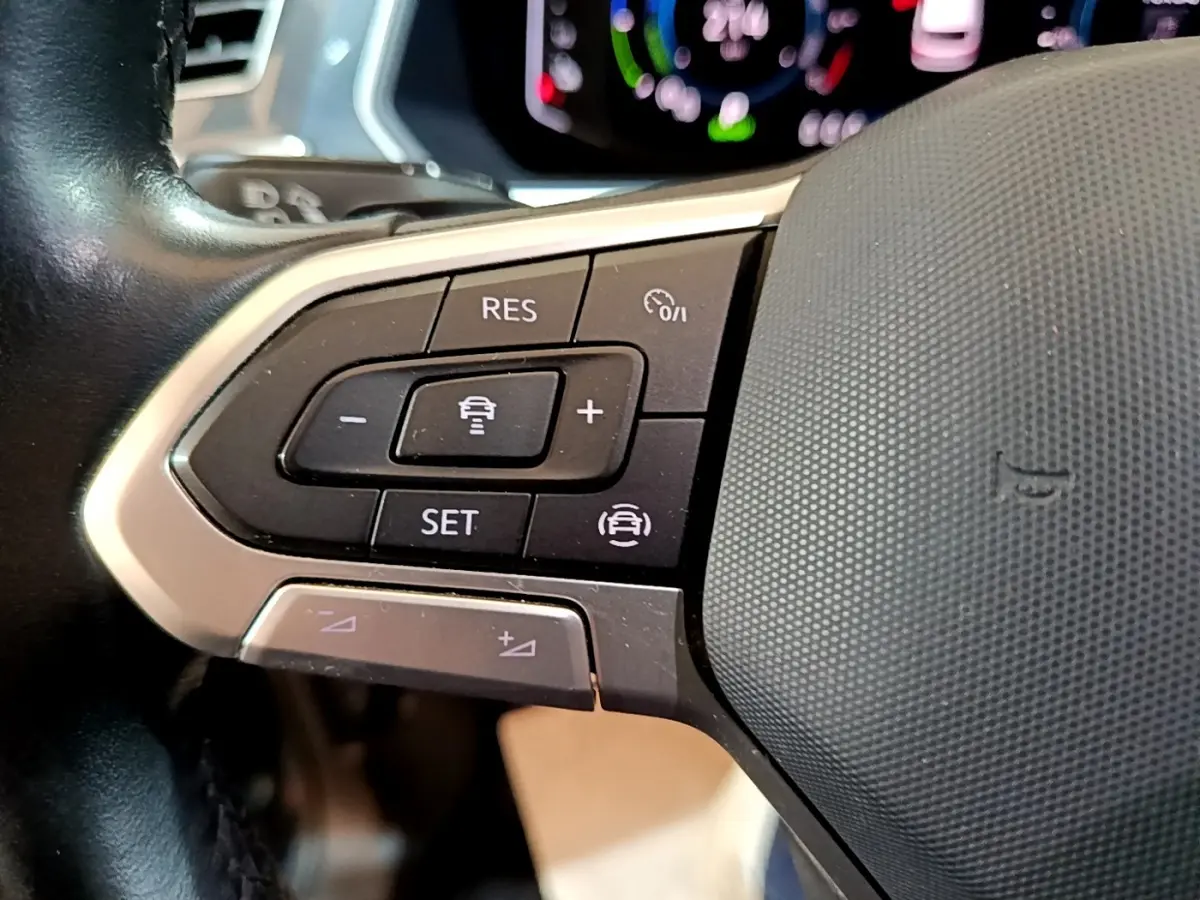 Gros plan sur les commandes de régulateur de vitesse au volant cuir du Volkswagen Tiguan bleu hybride rechargeable.