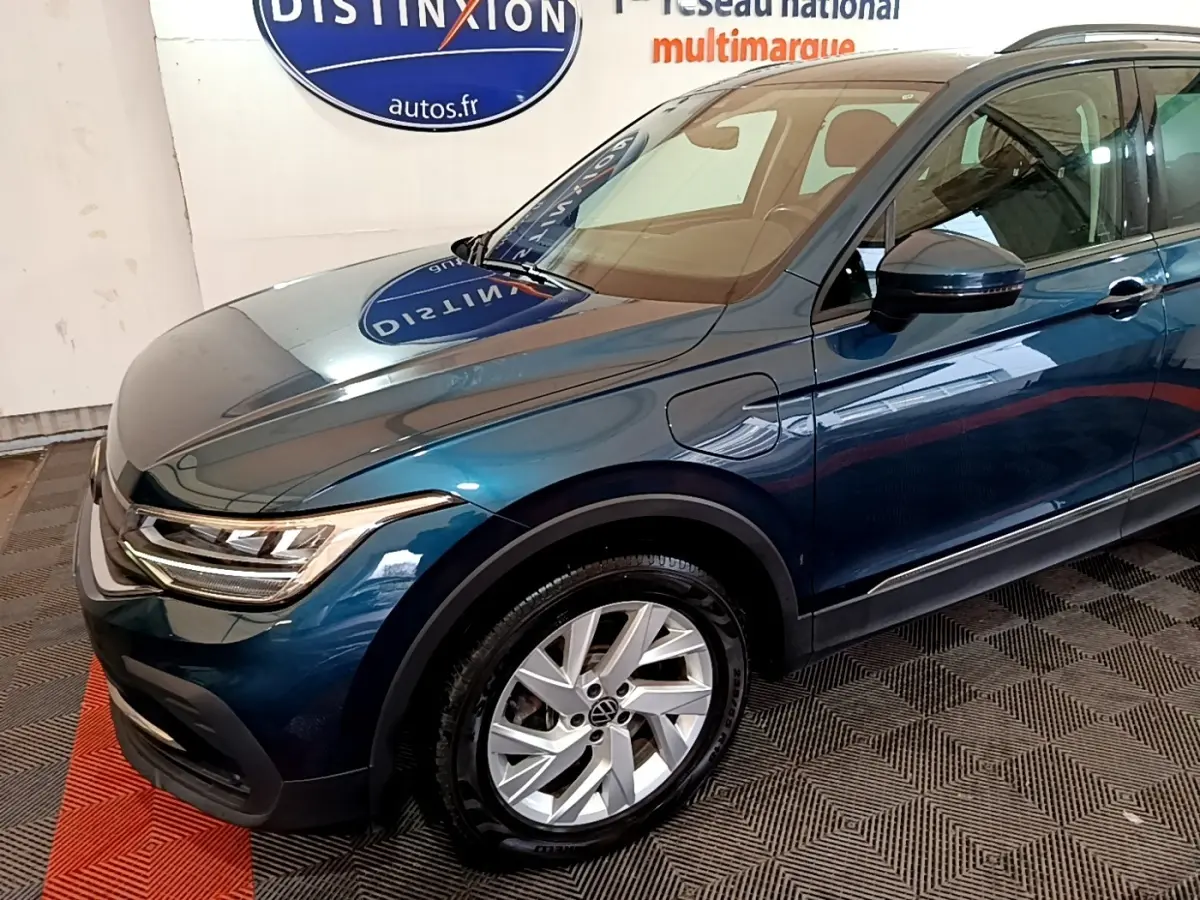 Vue 3/4 avant droit d'un Volkswagen Tiguan bleu hybride rechargeable avec jantes alliage et rétroviseurs noirs.