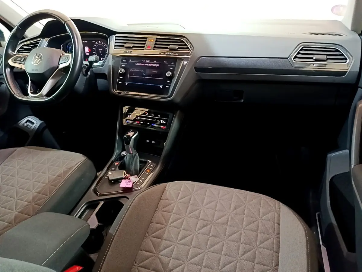 Vue intérieure avant du Volkswagen Tiguan 1.4 eHybrid 2021, sièges gris, tableau de bord avec écran tactile et volant cuir.