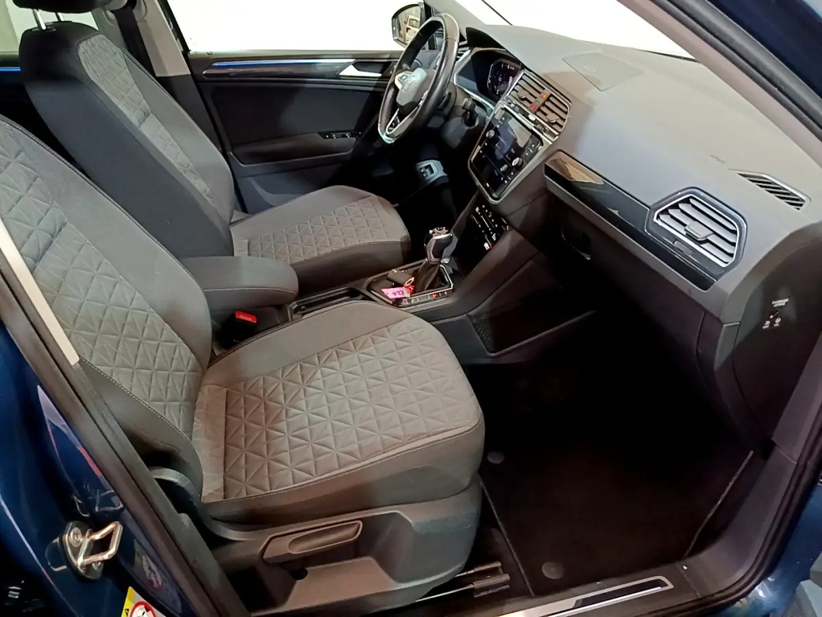 Vue intérieure côté conducteur du Volkswagen Tiguan bleu, montrant sièges tissu gris et tableau de bord moderne avec écran tactile.