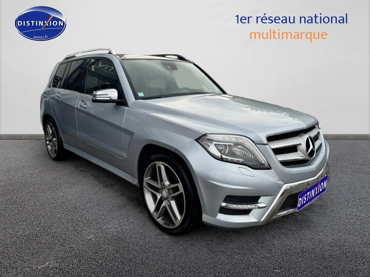 Vue 3/4 avant gauche d'un Mercedes GLK gris métallisé avec jantes alliage et barres de toit visibles.