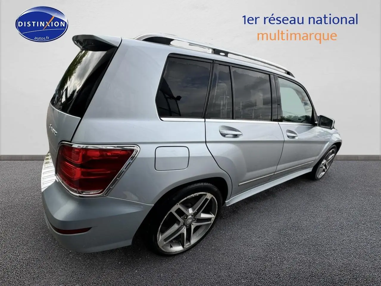 Vue 3/4 arrière droite d’un Mercedes GLK 350 4Matic gris métallisé avec barres de toit et vitres teintées.