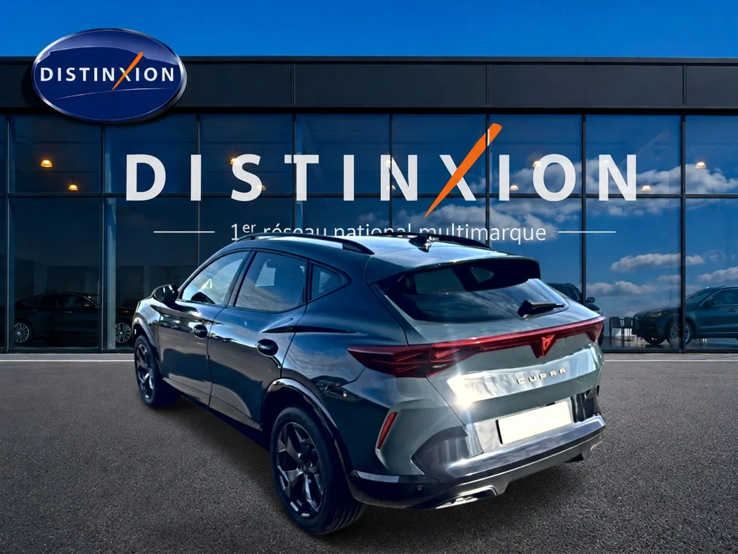 Vue 3/4 arrière droite du CUPRA Formentor bleu fjord avec feux arrière LED et jantes 18 pouces devant un showroom Distinxion.