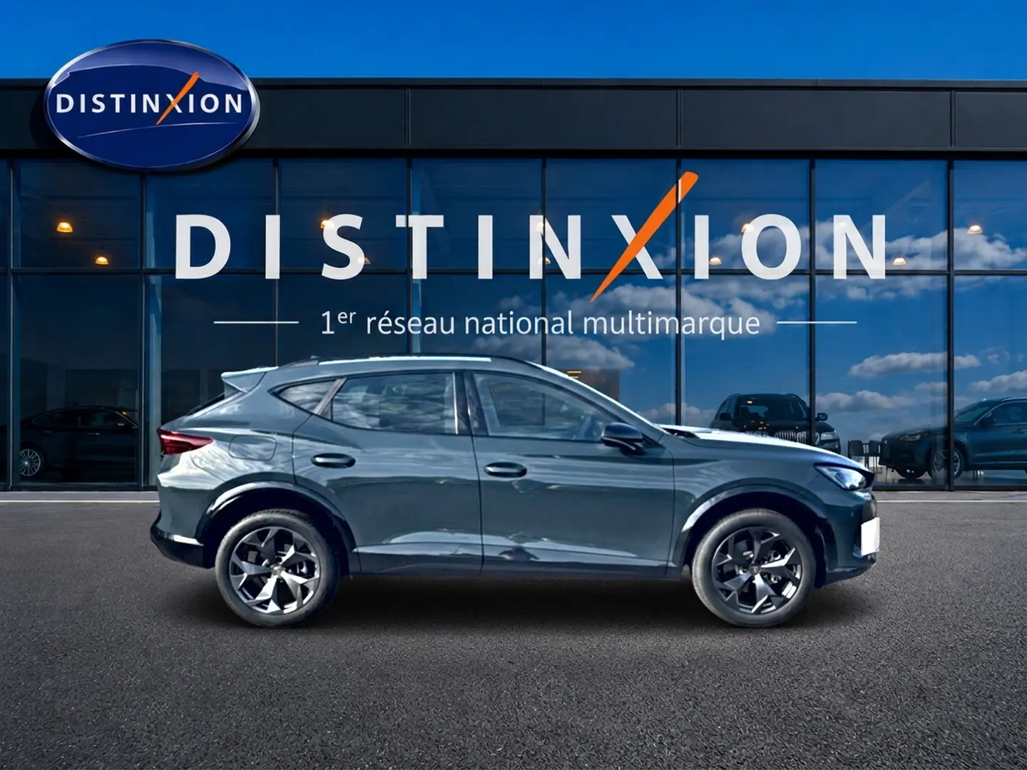 Vue latérale gauche du CUPRA Formentor 1.5 eTSI hybrid bleu fjord avec jantes 18 pouces devant une vitrine Distinxion.