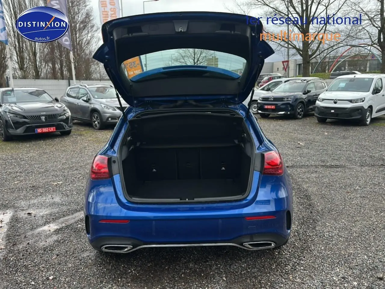 Vue arrière d'une Mercedes Classe A 180 AMG Line bleu avec coffre ouvert sur parking extérieur.