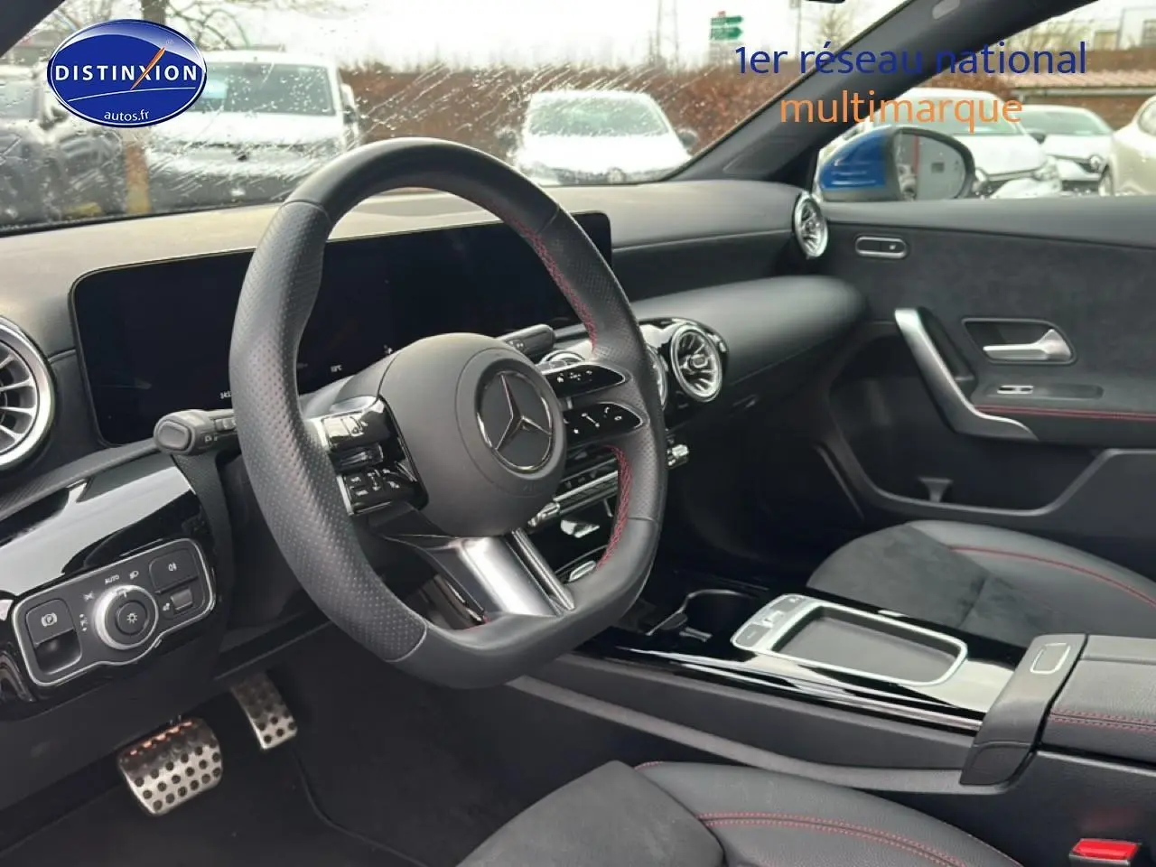 Intérieur noir avec volant sport cuir, tableau de bord numérique et surpiqûres rouges visibles côté conducteur.