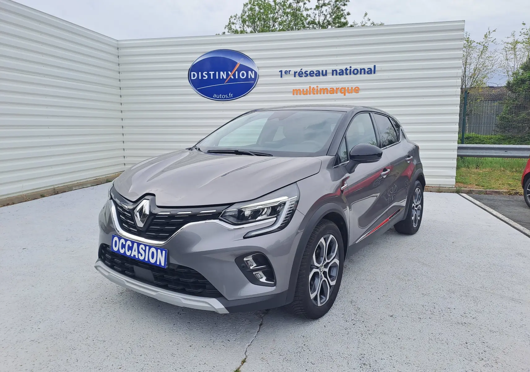 Renault Captur gris Cassiopée avec toit noir, vue 3/4 avant droit, sur parking devant un mur blanc.
