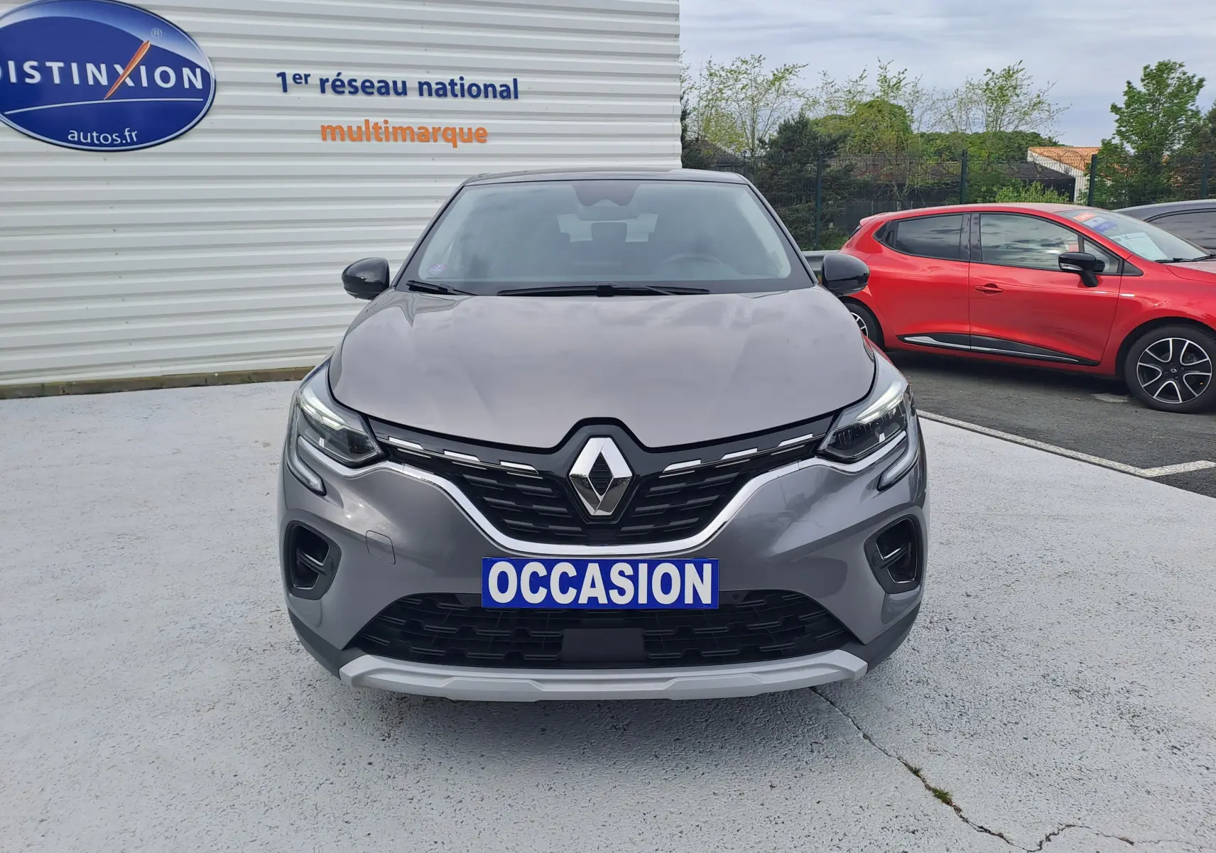Vue avant d'un Renault Captur gris Cassiopée avec toit noir, affichant une plaque "OCCASION" sur un parking extérieur.